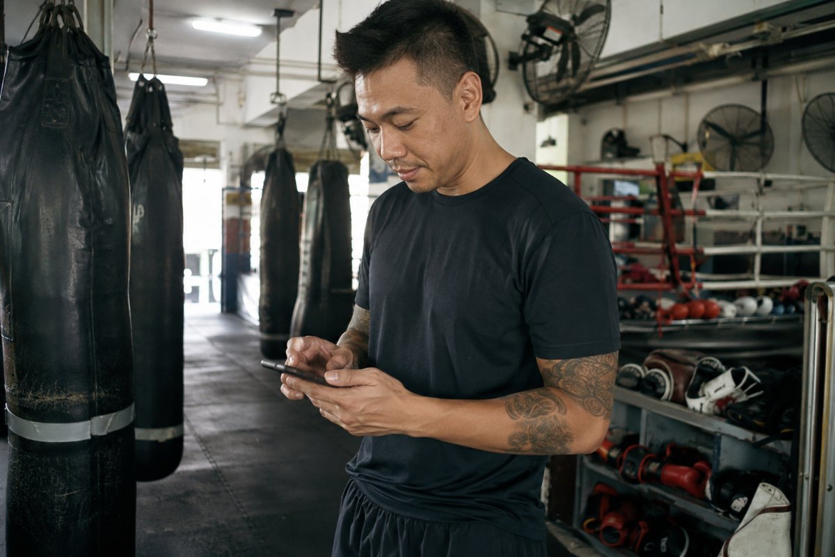 A Singapore gym owner smiling while replying to a membership enquiry on WhatsApp from a phone at the front desk