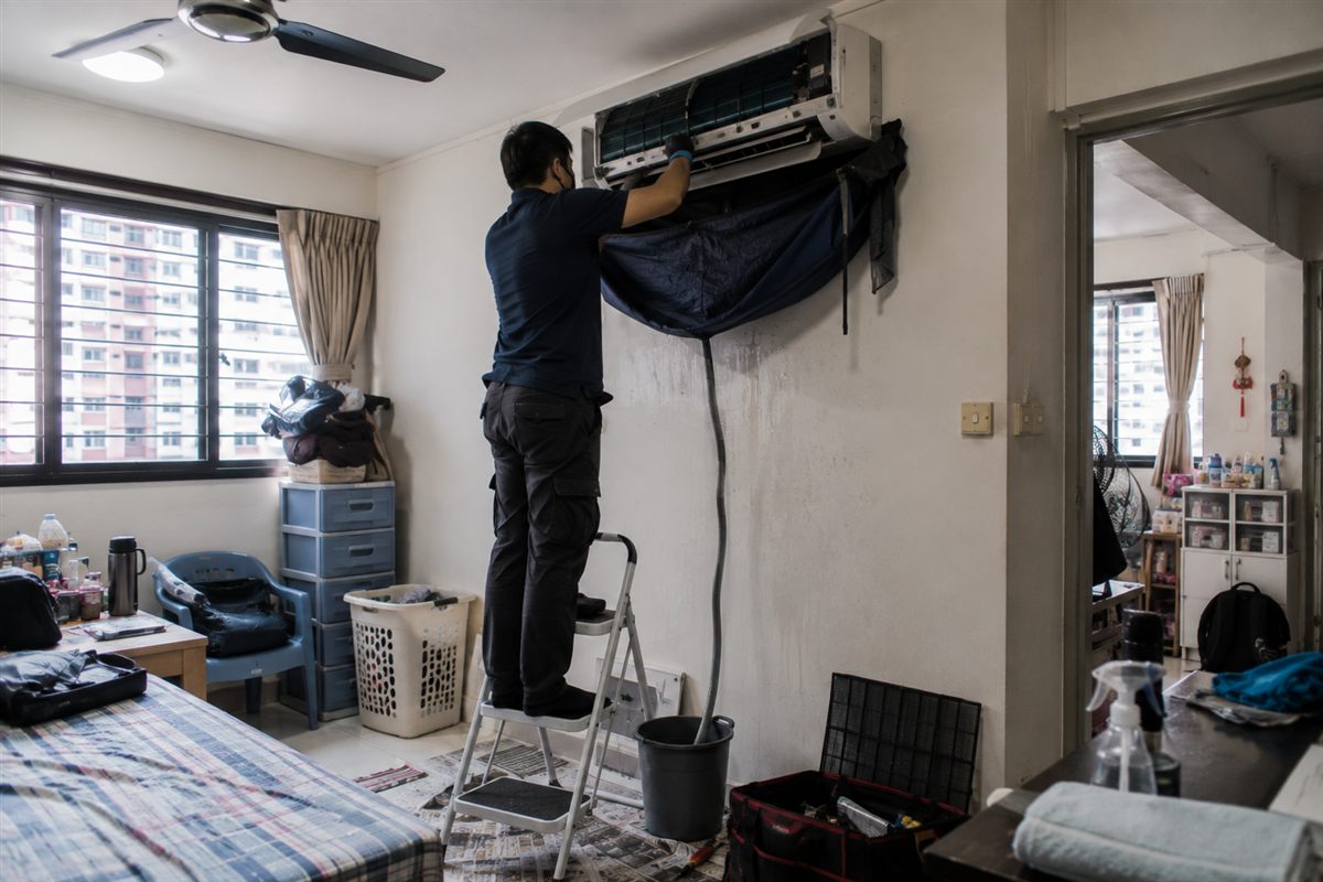 A Singapore aircon technician checking a WhatsApp job enquiry on a phone at a worksite